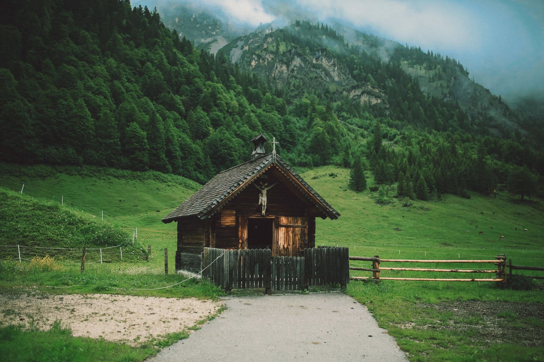 A weathered wooden chapel in a green valley under misty mountains