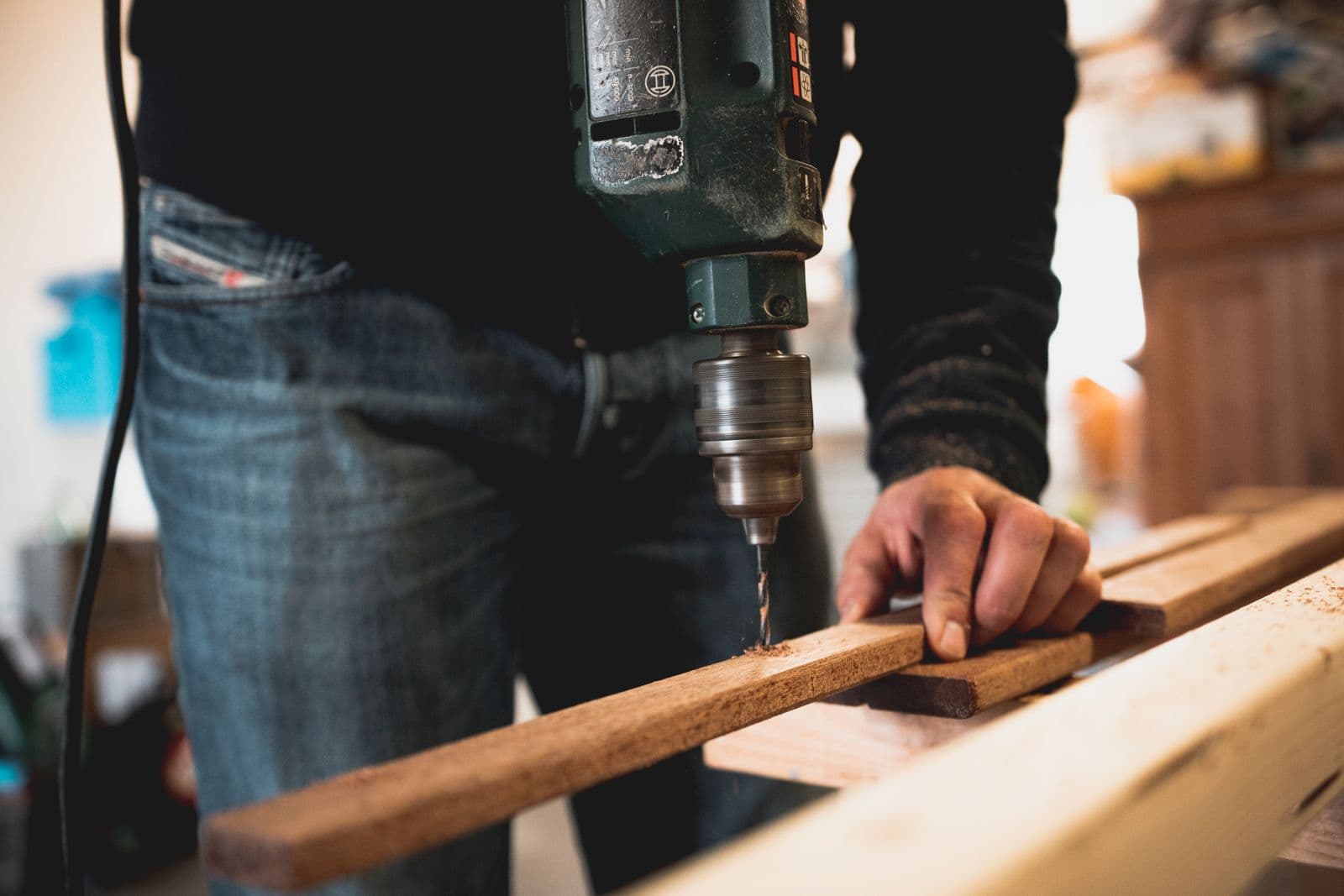 A craftsman’s hand holding a cedar plank while a drill bites into the grain